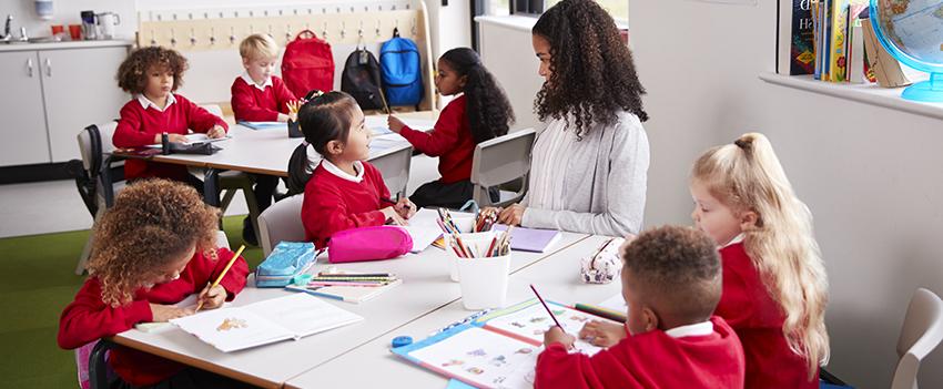 Teacher working with kids at tables in the classroom.